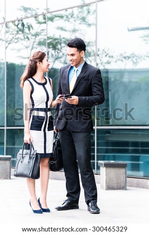 Asian business woman and man  with mobile phone in front of building