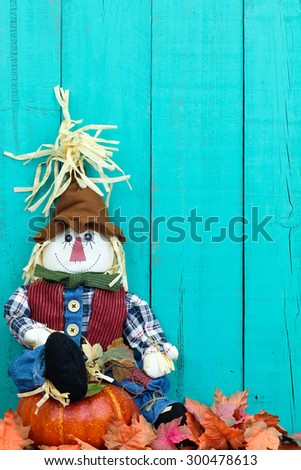 Scarecrow sitting on pumpkin by fall leaves and antique rustic teal blue wood background