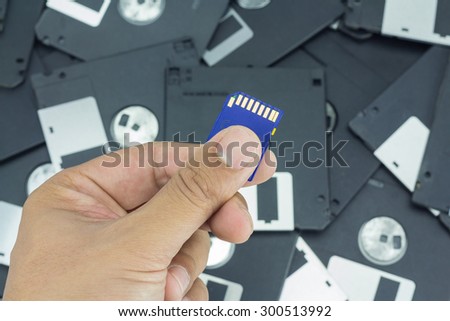 Hand holding SD card with floppy disk background