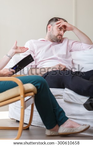 Photo of depressed man sitting on sofa during therapy