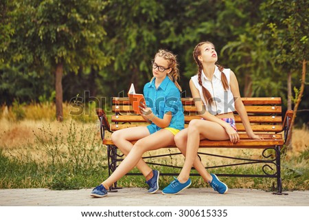Best friends are reading diary sitting on a bench in a summer park. Teen girl dressed in shorts and a shirt. On summer vacation. The concept of true friendship.