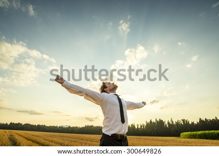 Half Body Shot of a Thankful Young Businessman Looking up the Sky with Wide Open Arms, Standing at the Open Field. Royalty-Free Stock Photo #300649826