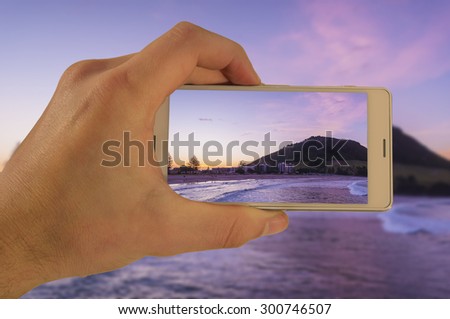Tourist hand holding smart phone, taking photo of Auckland New Zealand, Mt Maunganui