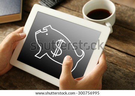 Money concept. Hands holding digital tablet with piggy bank image on it, close-up