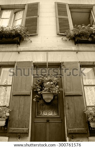Old house with wooden shutters and door decorated with geranium flower pots. Ile-de-France, France. Retro aged photo. Sepia.