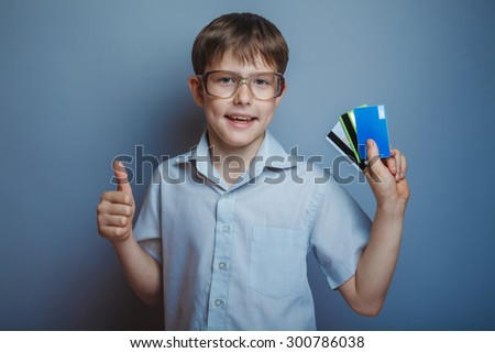 Teenage boy in glasses holding a credit card on a blue background of the photo studio