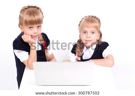Two cute curious girl twins on a white background looking at a laptop in fancy dresses. The picture with depth of field