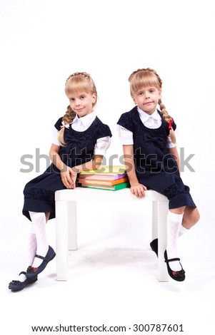 Curious cute little girl on white background sitting at desk with books in their hands in elegant dresses and smiling. The picture with depth of field