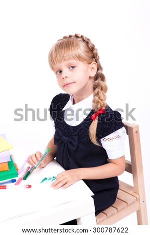 cute curious girl on white background sits at a table surrounded by books in a smart dress and draws. The picture with depth of field