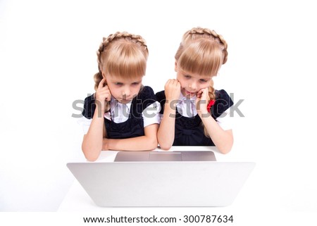 Two cute curious girl twins on a white background looking at a laptop in fancy dresses. The picture with depth of field