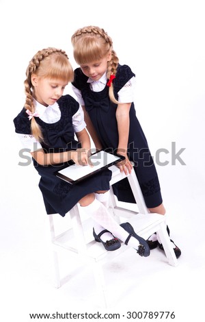 Two cute curious girl twins on white background sitting on a stool in smart dresses and holding in their hands the tablet. The picture with depth of field