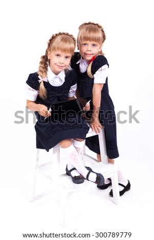 Two cute curious girl twins on white background sitting on a stool in smart dresses and holding in their hands the tablet. The picture with depth of field