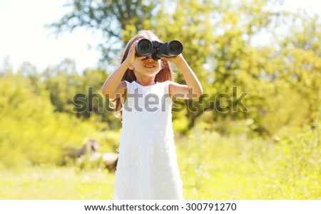 Little girl child looking through binoculars outdoors on sunny summer day