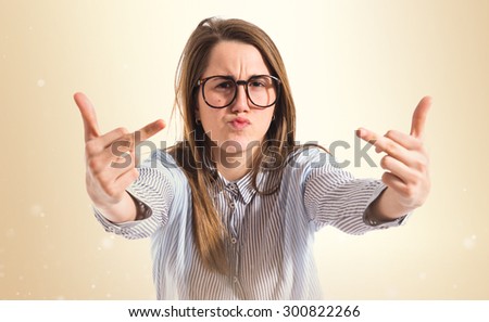 Cute girl making horn gesture over ocher background 