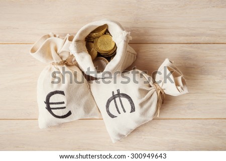 Coins in money bags on light wooden background, top view