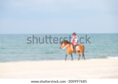 De focused or blurred picture of a man riding a brown horse along the beach for relaxation background