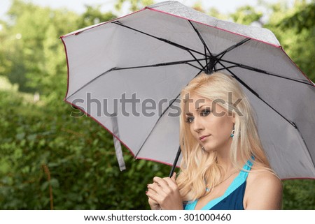 Beautiful blonde girl with umbrella in summer park after rain
