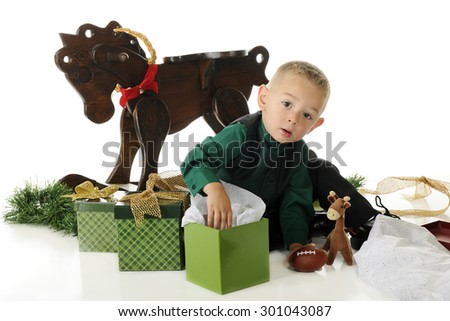 An adorable preschooler dressed up for Christmas, surrounded by gifts.  He's looking up as he digs into one box.  On a white background.