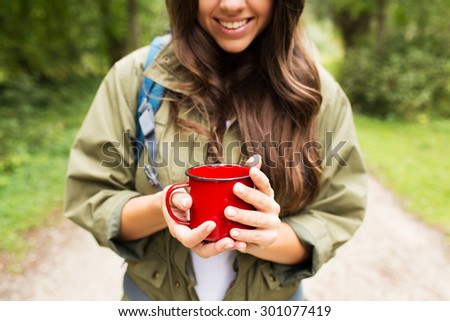 adventure, travel, tourism, hike and people concept - smiling young woman hiker with cup and backpack in forest