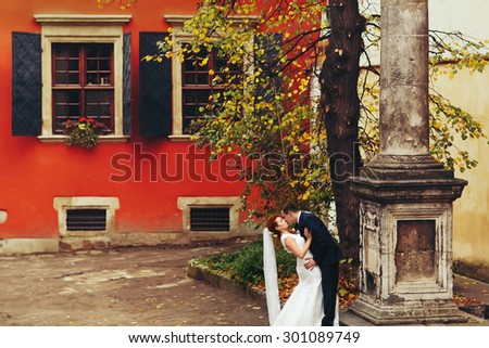 grom hugging bride with red hair outdoors background red wall  Lviv