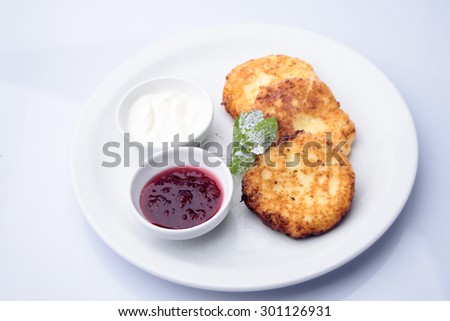 Delicious roasted cottage cheese pancakes with golden crust decorated with mint sour cream and berry jam on plate isolated on white, horizontal picture