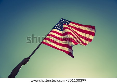 American flag with stars and stripes hold with hands against blue sky ( Filtered image processed vintage effect. )
