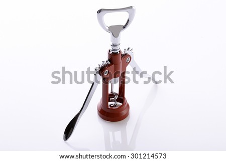 One wine opener made of silver colored metal and red plastic with sharp spiral standing and reflecting on table in studio isolated on white background copyspace, horizontyal picture