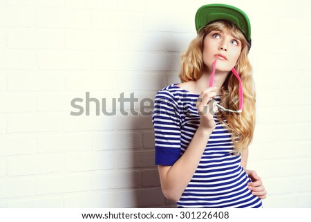 Joyful teen girl in casual clothes and sunglasses posing by a brick wall. Active lifestyle. Youth fashion. Studio shot. 