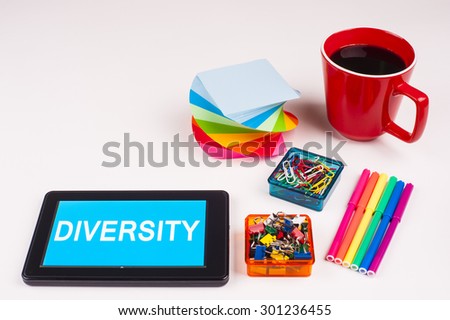 Business Term / Business Phrase on Tablet PC - Colorful Rainbow Colors, Cup, Notepad, Pens, Paper Clips, White surface - White Word(s) on a cyan background - Diversity