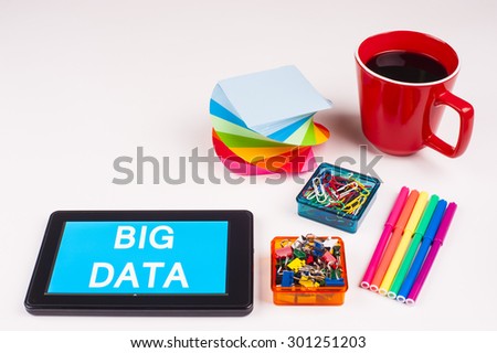 Business Term / Business Phrase on Tablet PC - Colorful Rainbow Colors, Cup, Notepad, Pens, Paper Clips, White surface - White Word(s) on a cyan background - Big Data