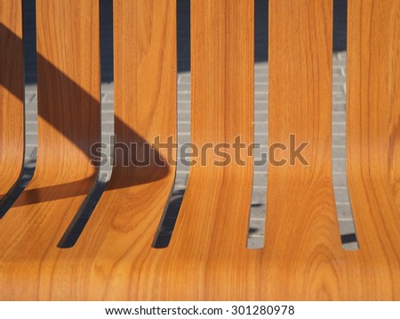 The seat is wooden benches on the street closeup and shadow from the back lit bright sun with pavement in the background