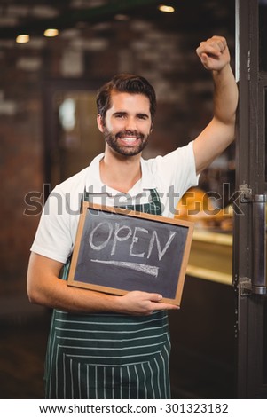 Portrait of a waiter showing chalkboard with open sign at the coffee shop