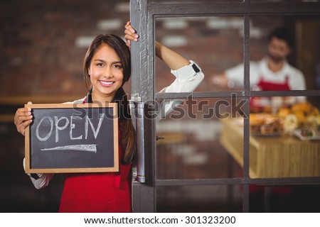 Portrait of waitress showing chalkboard with open sign at coffee shop
