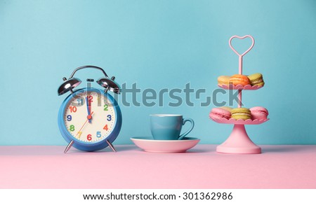 Cup of coffee and alarm clock on the blue and pink background with macarons 