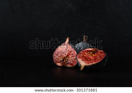 A still life arrangement of very ripe and juicy figs in a three piece grouping on black slate against a chalkboard background. 