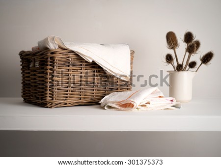 Wicker Basket with linen inside, on a shelf with a rustic bottle and dried teasel plant Royalty-Free Stock Photo #301375373