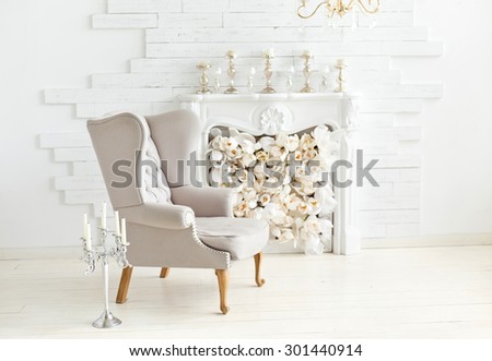 Elegant soft arm-chair near a fireplace. Luxury interior in white colors. Armchair with fabric upholstery Royalty-Free Stock Photo #301440914