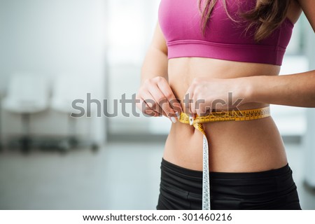 Slim young woman measuring her thin waist with a tape measure, close up Royalty-Free Stock Photo #301460216