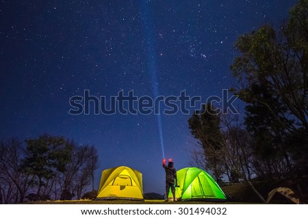 a photographer point a flashlight in to the sky between camp in forest at night with star