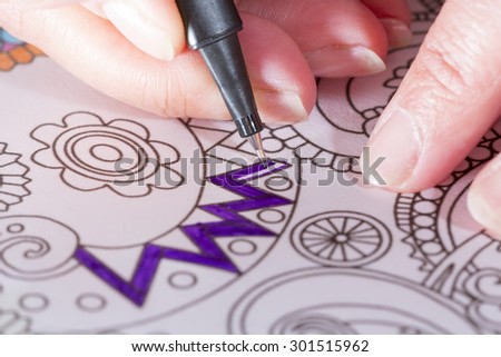 An image of a new trendy thing called adults coloring book. In this image a person is coloring an illustrative and detailed pattern for stress relieve for adults with a color pencil.