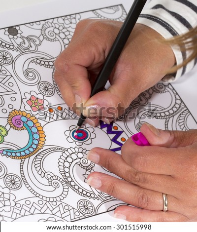 An image of a new trendy thing called adults coloring book. In this image a person is coloring an illustrative and detailed pattern for stress relieve for adults with a color pencil.