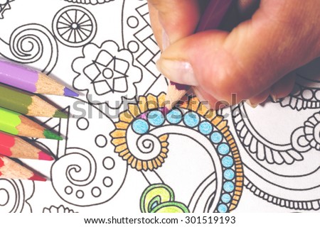 An image of a new trendy thing called adults coloring book with a vintage twist.. In this image a person is coloring an illustrative and detailed pattern for stress relieve for adults.