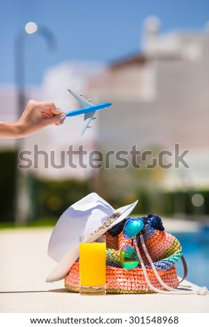 Colorful beach bag, glass of juice, straw hat and airplane model in female hand on summer vacation