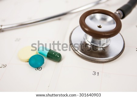 stethoscope with pill on calendar note.