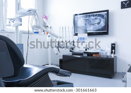 Dentists chair and tools with x-ray picture on TV in the background. Dental care, dental hygiene, checkup and therapy concept. Royalty-Free Stock Photo #301661663