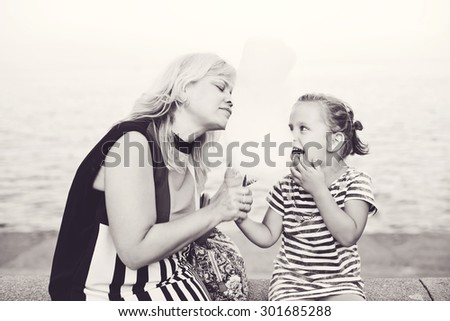 woman and little girl eating a cotton candy next to the sea