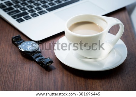 laptop with watch and cup of coffee on brown wooden table. 
