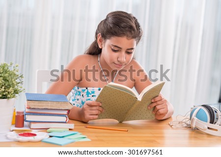 Hispanic schoolgirl sitting at the table and reading a book