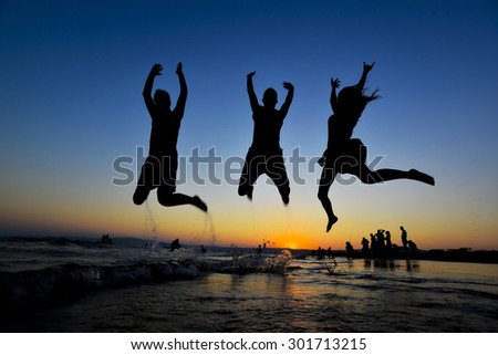 Silhouette of young group of people jumping in ocean at sunset 