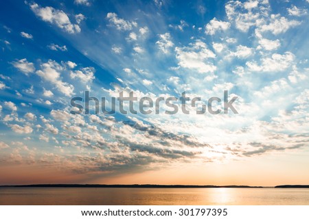 Clouds and sun rays over lake at sunrise Royalty-Free Stock Photo #301797395